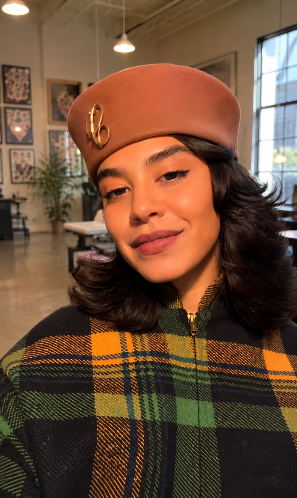 Siara Mencia in her East Harlem studio, wearing a rust-coloured beret and a green and orange plaid jacket, with framed flash sheets on the wall behind her.