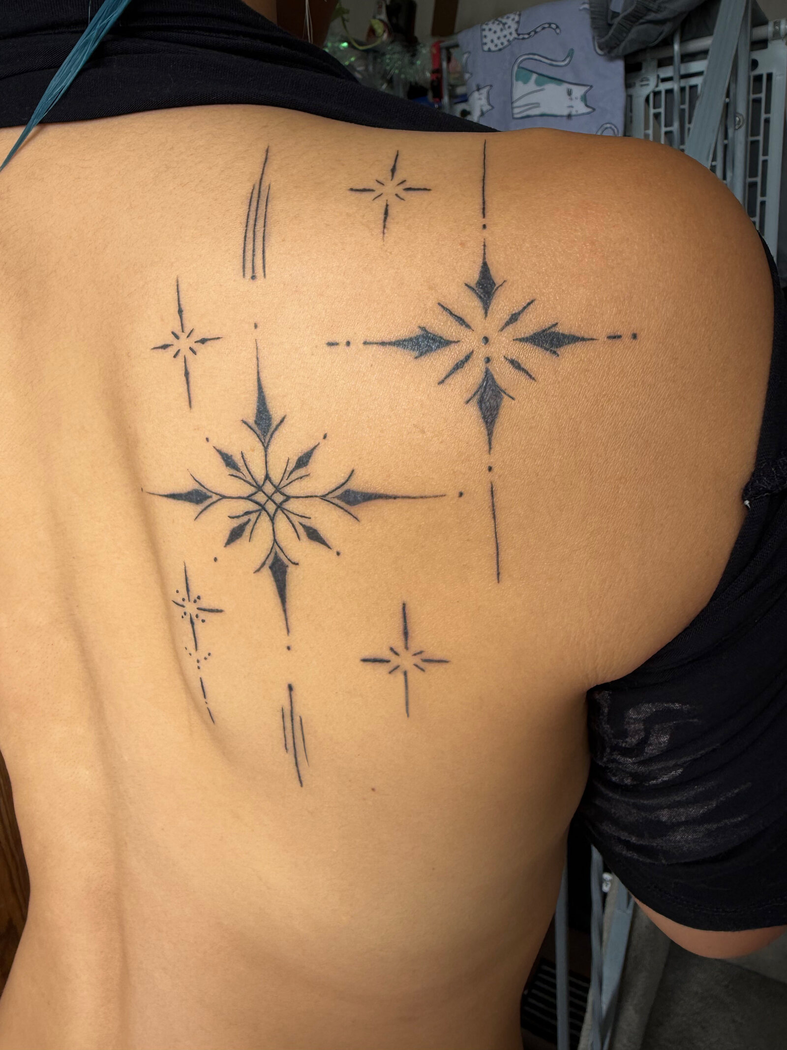Fine-line ornamental star and spark motifs arranged across a client's upper back and shoulder blade in black ink.