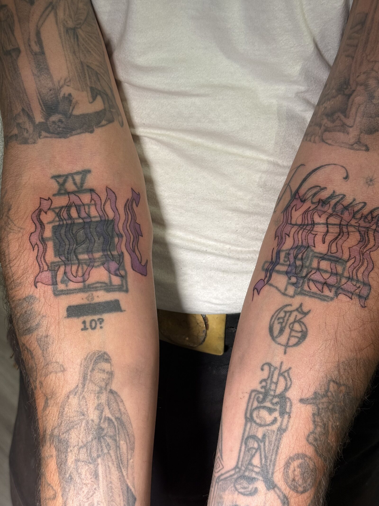 Both forearms shown together, each with a matching stained-glass window motif in pink and purple flames above older black and grey work.