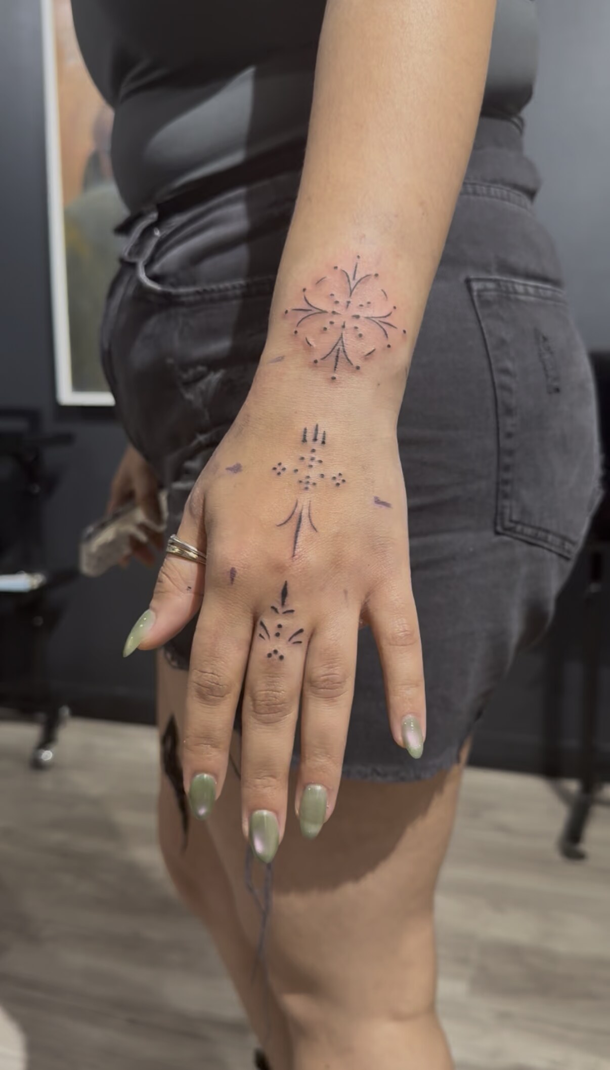 Delicate ornamental blackwork on a hand: a symmetrical floral motif on the wrist, a dotted crown on the back of the hand, and a small ornament on the finger.